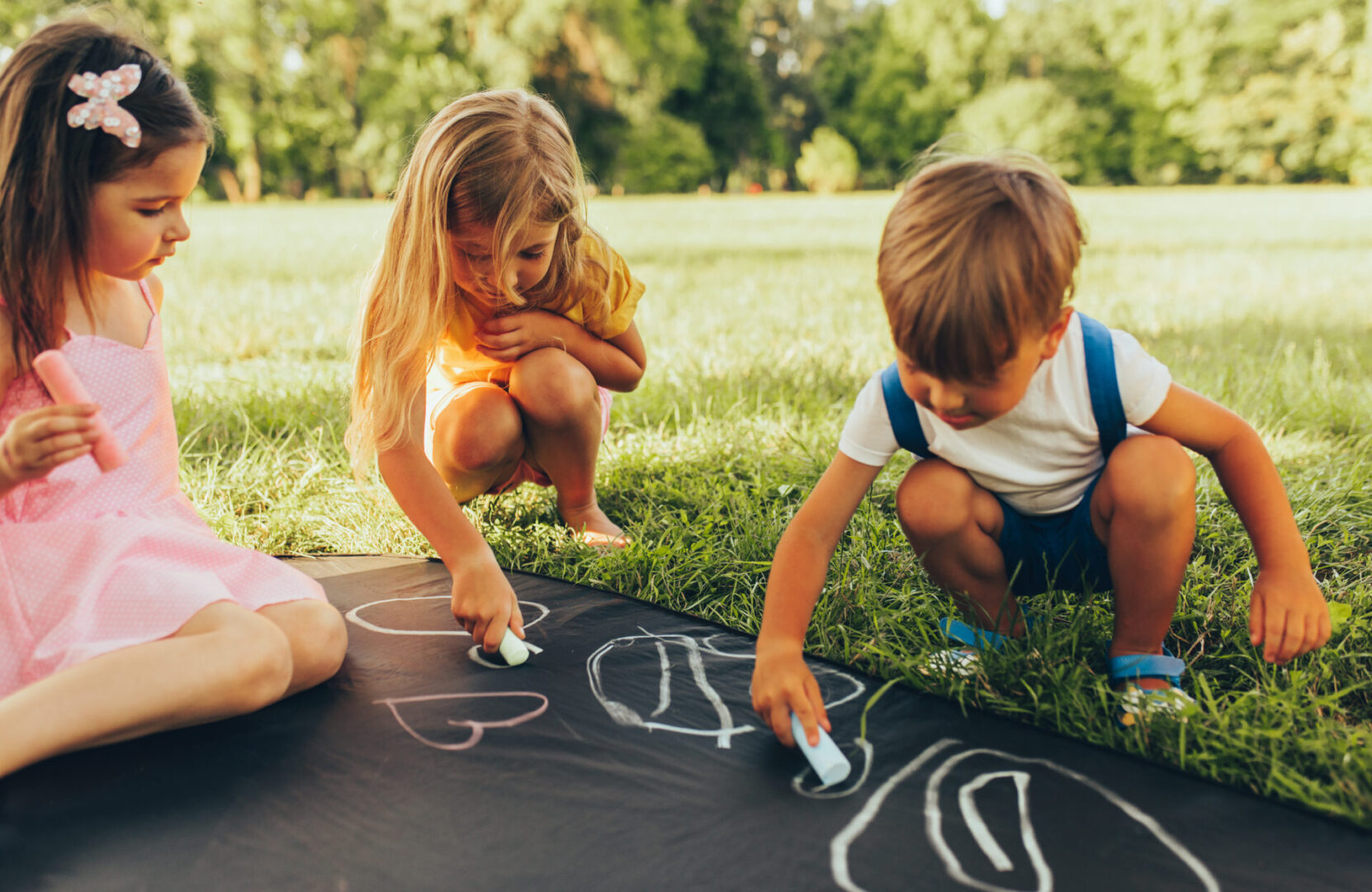 Three children playing with chalk on a blackboard in a park, showcasing the nurturing qualities of the Cancer sign.