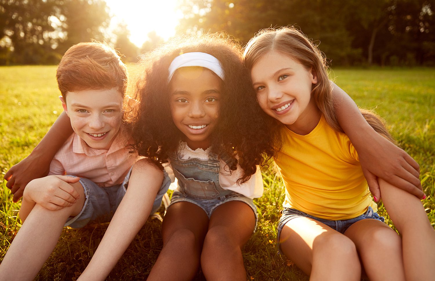 Three Taurus kids sitting on the grass and smiling at the camera.