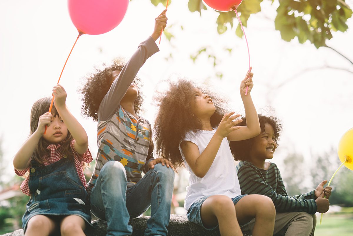 A group of children sitting on a rock and holding balloons, showcasing qualities of the Virgo Sign.